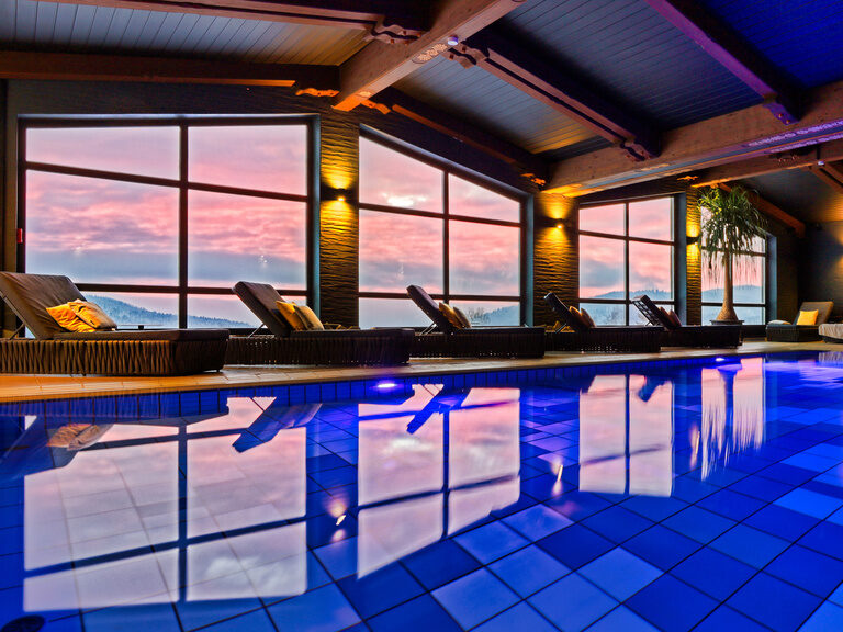 Der elegante Panorama-Hallenbad im natura SPA mit blauen Pool, Liegemöglichkeiten und toller Aussicht auf den Bayerischen Wald